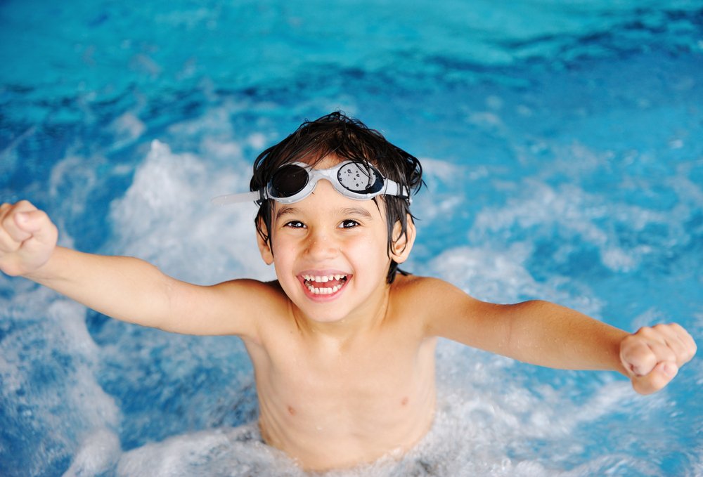 Young boy in pools with goggles smiling