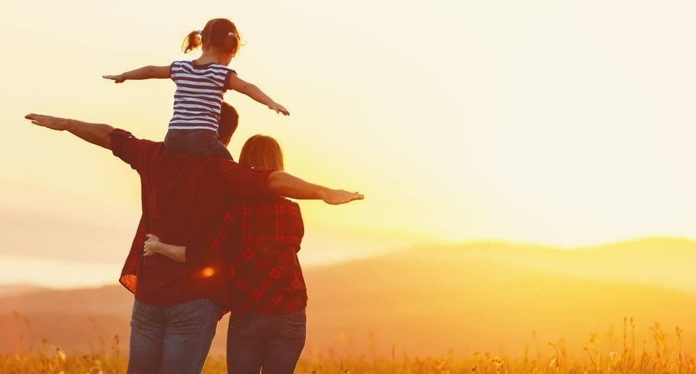 Family of three with arms out like airplanes enjoying a mountain sunset